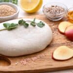 Easy and stretchy vegan mozzarella, on a wooden chopping board with some apples, sunflower seeds, lemon, psyllium husk and cider vinegar