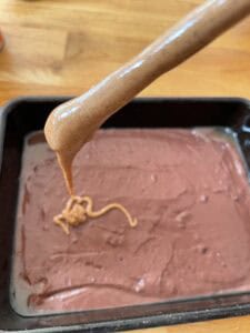 peanut butter being hold in a chopstick to pour into brownie batter