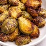 Roasted brussels sprouts topped with some nutritional yeast on a white bowl