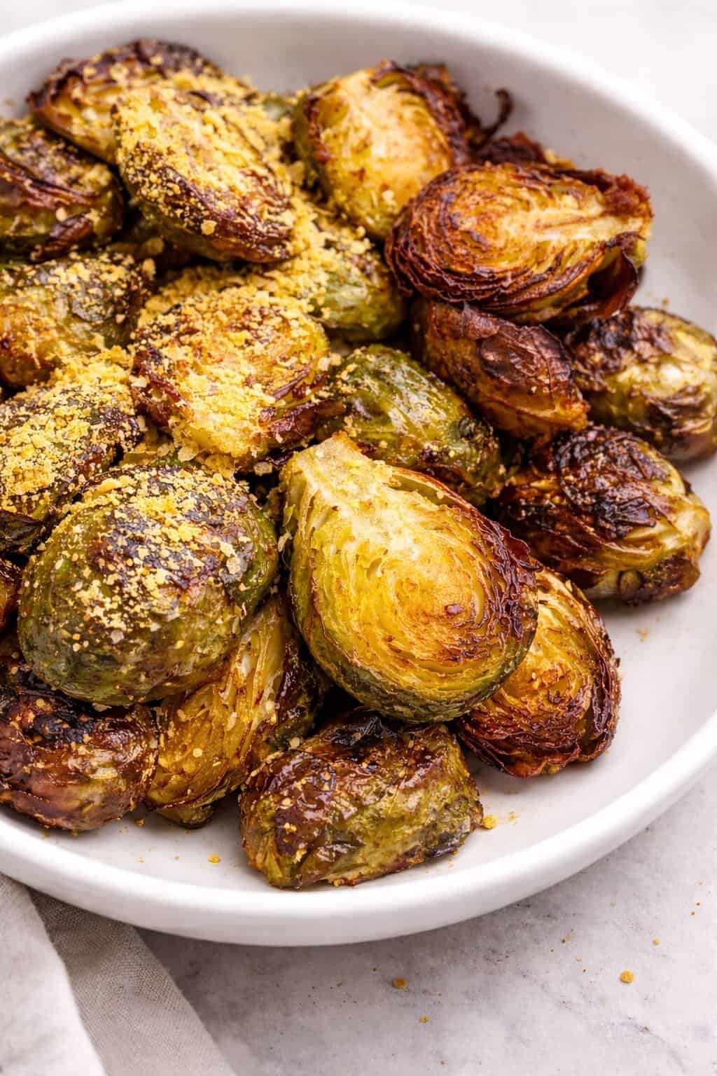 Roasted brussels sprouts topped with some nutritional yeast on a white bowl